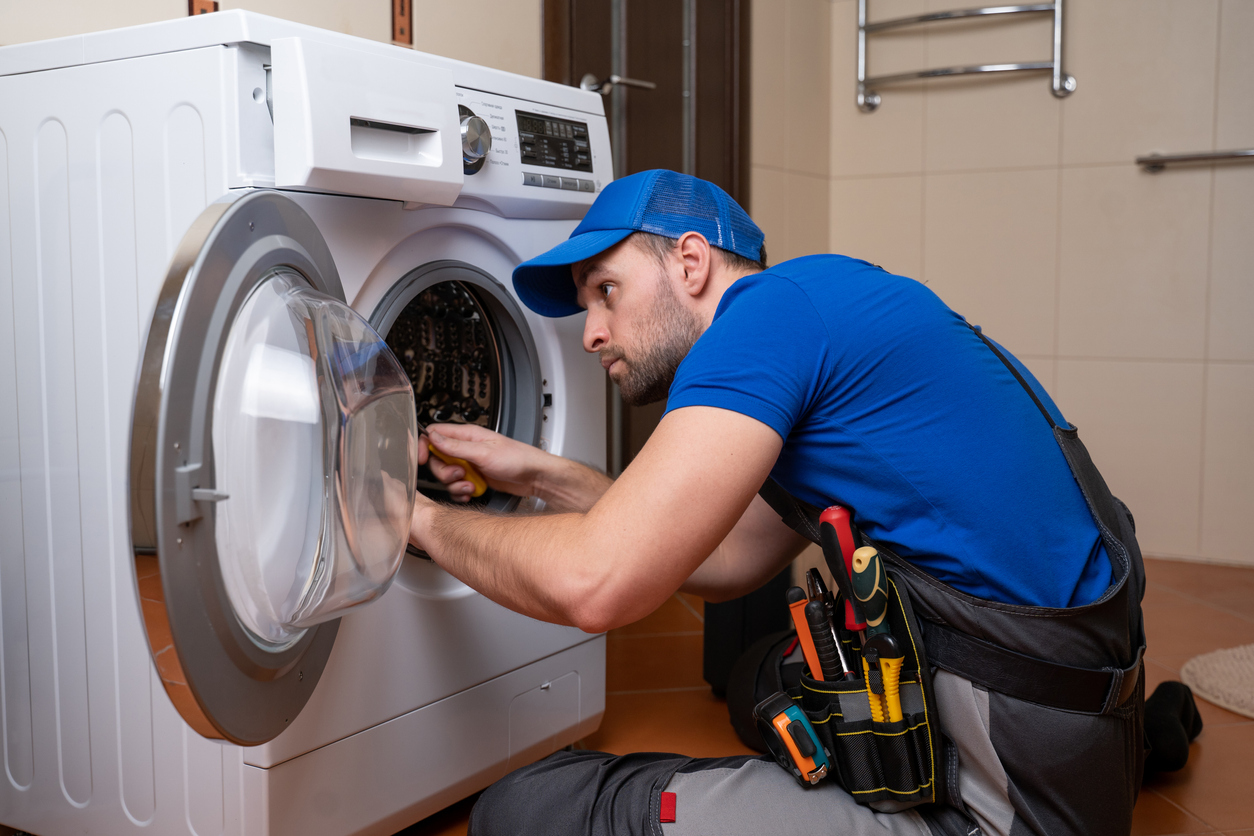 Working man plumber repairs a washing machine in home. Washing machine installation or repair. plumber connecting appliance